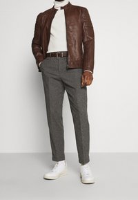 Hnědá kožená bunda, bílý rolák, šedé kalhoty s vzorem, hnědý pásek a bílé tenisky. Texturovaný materiál, přiléhavý střih.