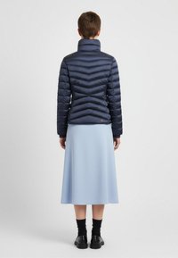 Marinblå puffjacka med chevronstygn och hög krage, kombinerad med en ljusblå kjol. Svarta skor och strumpor kompletterar utseendet.