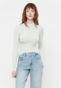 Haut à manches longues à côtes de couleur vert menthe clair avec un col montant, associé à un jean taille haute bleu délavé, présentant des détails de couture subtils.