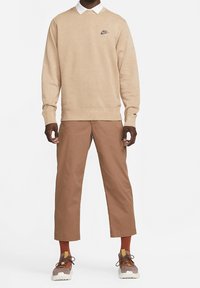 Beige sweatshirt with Nike logo, white collar, paired with brown cropped pants. Sneakers are gray and brown with orange accents and white soles.