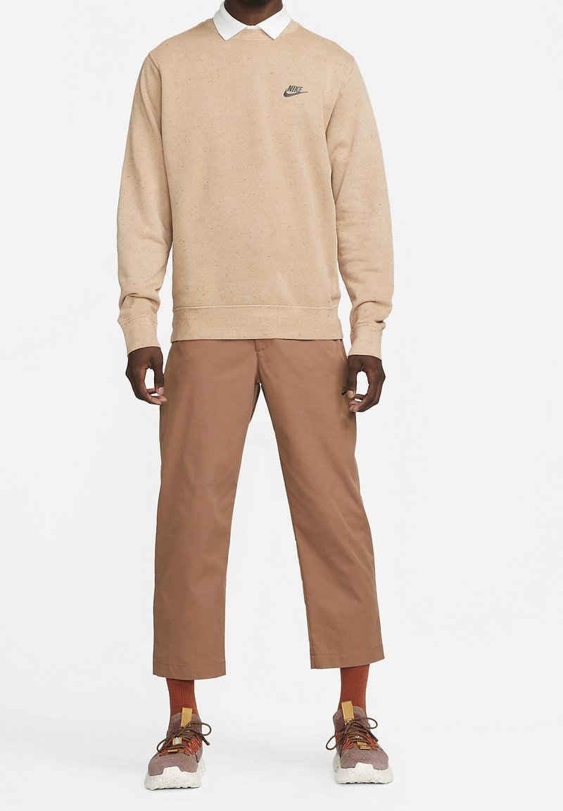 Beige sweatshirt with Nike logo, white collar, paired with brown cropped pants. Sneakers are gray and brown with orange accents and white soles.