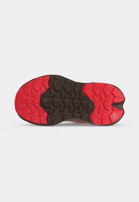 Semelle d'une chaussure de course avec une bande de roulement en caoutchouc rouge et noir présentant de profondes rainures pour la traction, montrée sur un fond blanc uni.