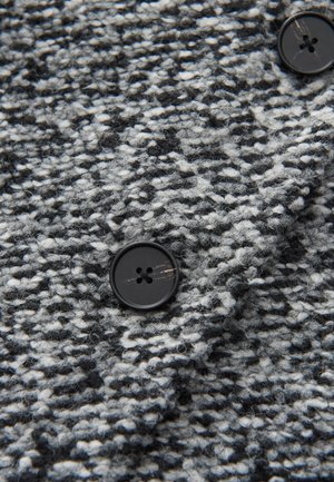 Tissu texturé gris et noir avec un motif tissé ; présente un grand bouton noir à quatre trous.