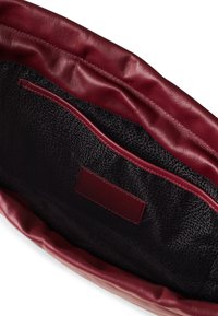 Innenansicht einer roten Lederhandtasche mit glatter Textur, schwarzem gemustertem Futter und einer Innentasche. Etikett an der Seite eingestickt.