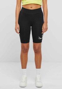 Schwarze Radshorts aus dehnbarem Stoff, mit hohem Bund und einem weißen grafischen Design am linken Oberschenkel.