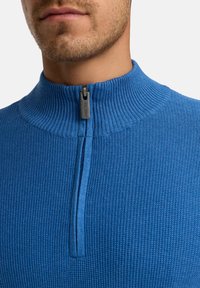 Blau gerippter Pullover mit hohem Kragen und halber Reißverschlussöffnung. Strukturierter Stoff mit einem glatten Reißverschluss-Zugdetail.