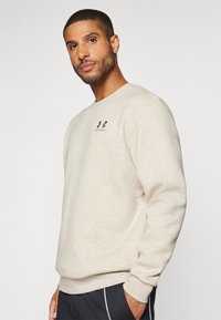 Sweatshirt bej, realizat dintr-un material tricotat moale, având un guler rotund și un mic logo negru pe piept. Design confortabil și casual.