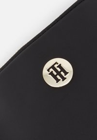 Czarny portfel z materiału o teksturowanym wykończeniu, z okrągłym złotym emblematem z wyrytymi inicjałami, podkreślający elegancki design.
