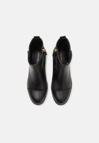 Bottes chelsea en cuir noir avec un bout rond, finition lisse, détails de zip doré et panneau supérieur mat contrastant. Côtés élastiques pour un enfilage facile.