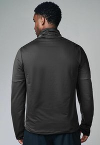 Langslippende zwarte sportjack met hoge kraag, gladde textuur en een aansluitend ontwerp, met duimopeningen en een rechte zoom.