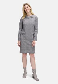 Abito a scacchi grigio con maniche lunghe, scollo a cowl e due tasche frontali. Abbinato a stivaletti grigi alla caviglia. Tessuto liscio e textured.