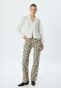 Blouse peplum blanche texturée avec bouton sur le devant, associée à un pantalon beige imitant le serpent et des bottines noires à talons pointus.