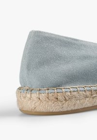 Hemelsblauwe canvas espadrille met een jute touwzool, met een ronde vorm en zichtbare stiksels langs de rand.