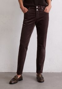 Bruine corduroy broek met een slim fit, voorzien van voorzakken, twee witte knopen en een gladde textuur. Gecombineerd met donkere loafers.