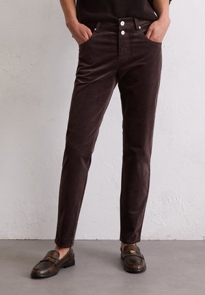 Bruine corduroy broek met een slim fit, voorzien van voorzakken, twee witte knopen en een gladde textuur. Gecombineerd met donkere loafers.
