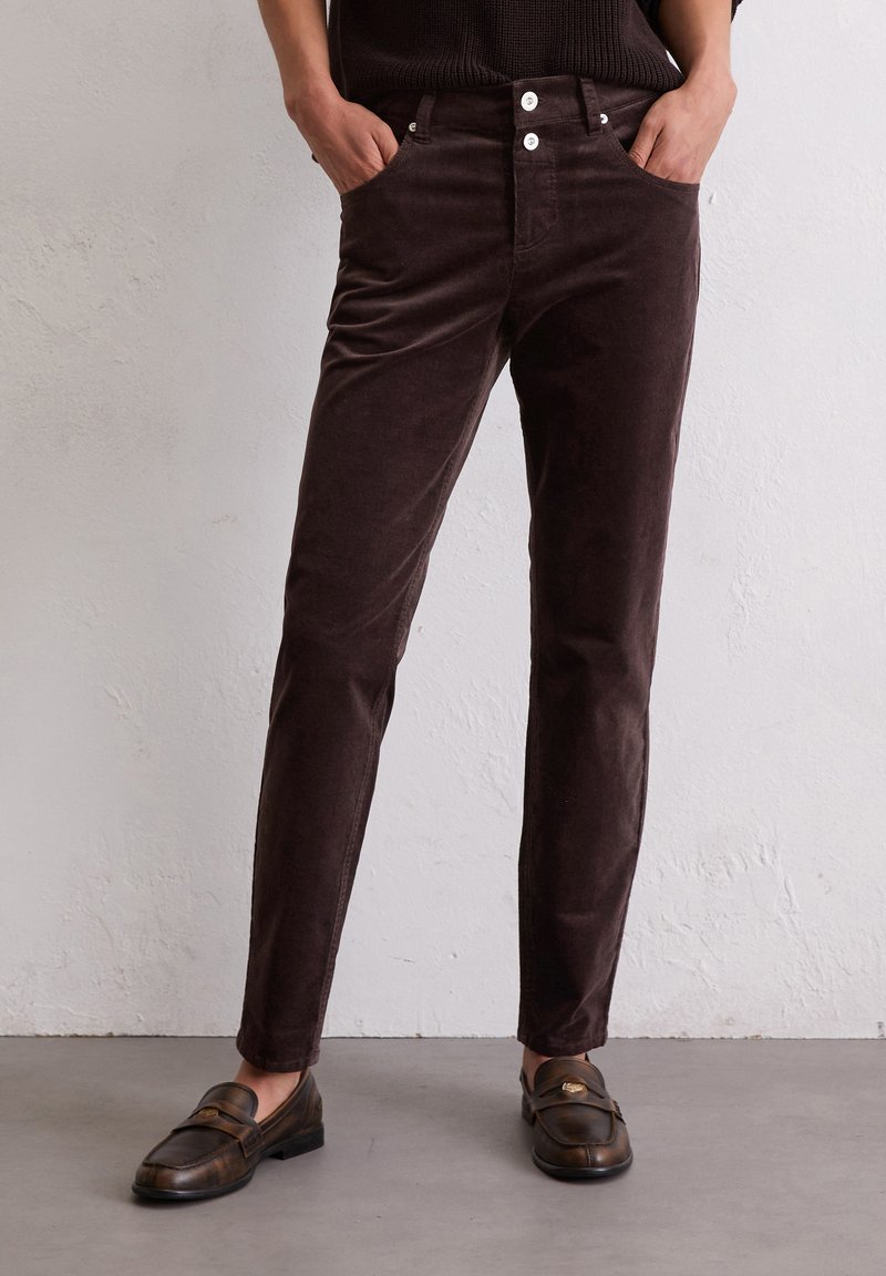 Bruine corduroy broek met een slim fit, voorzien van voorzakken, twee witte knopen en een gladde textuur. Gecombineerd met donkere loafers.