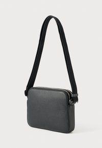 Černá kožená kabelka přes rameno s texturovaným povrchem, obdélníkovým tvarem a nastavitelným popruhem. Má zip na zavírání a minimální kovové doplňky.