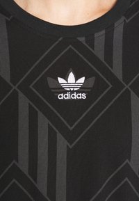 Camisa negra de Adidas con patrones geométricos oscuros y un logo de trébol blanco de Adidas centrado debajo del cuello.
