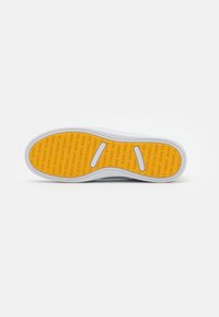 White sneaker sole with a textured, orange inner surface featuring repeated text "TOMMY JEANS." Two cutouts for flexibility are visible.