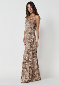 Maxi dress in a brown animal print, featuring spaghetti straps, a fitted bodice, and a flowing skirt with a smooth texture.