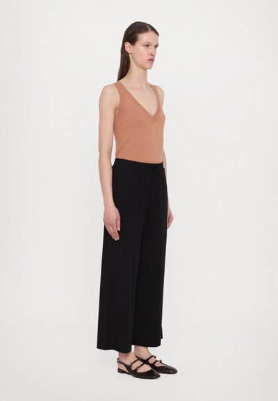 Brown sleeveless top with a V-neck, paired with loose black trousers and black slingback shoes, featuring a textured pattern.