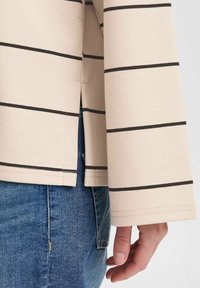 Haut beige rayé avec des lignes horizontales noires, une coupe droite et une fente sur le côté, associé à un jean en denim bleu.