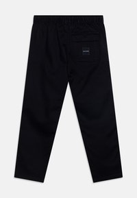 Czarne spodnie o luźnym kroju z elastycznym pasem, tylną kieszenią i małą metką. Gładka tkanina bez widocznych wzorów.