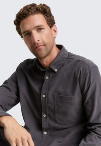 Camisa abotonada de color gris carbónico hecha de una tela suave, que cuenta con un bolsillo en el pecho, botones en la parte delantera y un cuello estructurado.