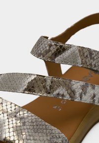 Πέδιλα με μοτίβο δέρματος φιδιού σε γκρι και καφέ αποχρώσεις, με σταυρωτούς ιμάντες και λεία, καφέ σόλα. Ορατή λεπτομερής υφή.