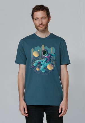 Teal cotton t-shirt featuring a graphic of an astronaut in shades of purple and turquoise against a geometric background with yellow accents.