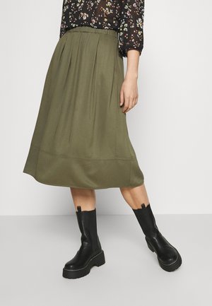 Olivengrøn plisseret midi-nederdel med glat tekstur; kombineret med sorte, chunky ankelstøvler med platformssål og en løkke bagpå.