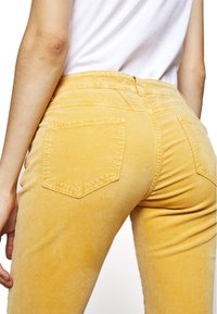 Pantalones de pana amarillos con una textura suave, que cuentan con bolsillos traseros con solapas puntiagudas y una cintura de talle medio.