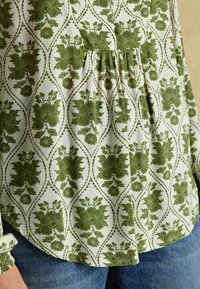 Zaļš ziedu raksta krekls ar baltu fonu, kam ir sak Gathered dizains un pogu detaļas. Mīksta auduma, nedaudz strukturēta.