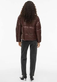 Smešak smeđi puffer kaput s sjajnim finišem, s horizontalnim jastučićima, širokim rukavima i skraćenim dizajnom, nosi se s tamnosivim trapericama.