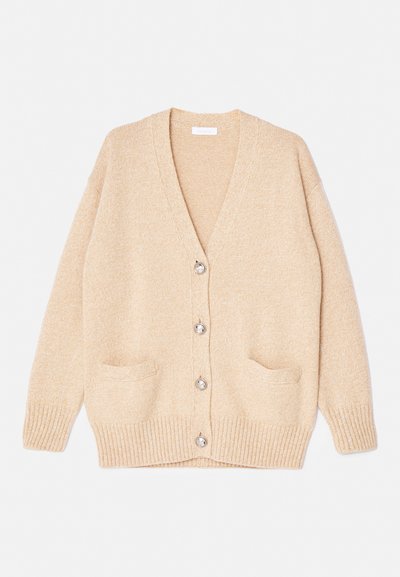 Μπεζ πλεκτό κοντό μπουφάν με V-λαιμό, πέντε ασημένια κουμπιά και δύο μπροστινές τσέπες. Διαθέτει ριμπ μανσέτες και στρίφωμα για επιπλέον λεπτομέρεια.