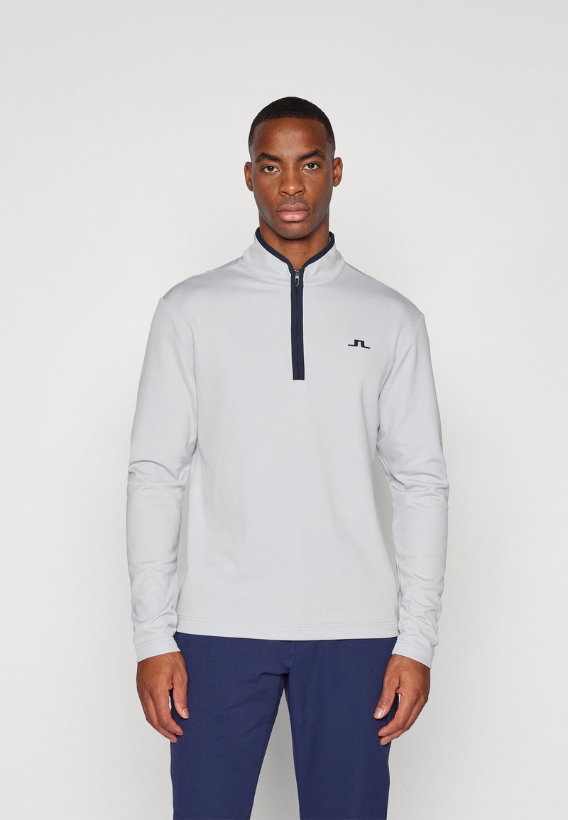 Lys grå zip-up fleece-genser med høy krage, lange ermer og en marineblå glidelås. Har en liten logo på brystet.