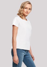 White short-sleeve t-shirt with a round neckline, made of cotton. Simple design, relaxed fit. Paired with blue denim jeans.