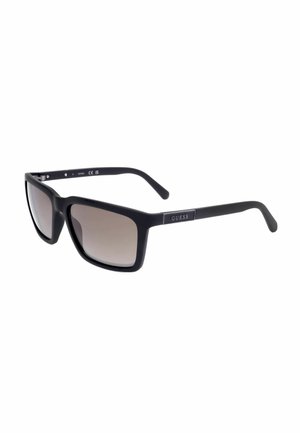 Occhiali da sole rettangolari neri con lenti sfumate grigie e logo "GUESS" sulle aste, inclinati verso destra su sfondo bianco.