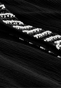 Tel fabric negro con un acabado texturizado, que presenta una banda de cuentas de alternando cuentas negras y blancas dispuestas en un patrón geométrico.