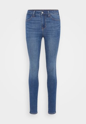 Skinny jeans in medium blue denim, featuring a high waist, five pockets, and subtle fading. The fabric has a smooth texture and slight stretch.