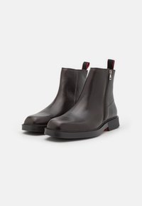 Schwarze Leder-Stiefeletten mit strukturierter Oberfläche, seitlichem Reißverschluss und einer stabilen schwarzen Sohle. Mit roten Akzenten am Kragen und an der Ferse.