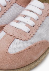 Růžové semišové a bílé bavlněné tenisky s vlnitými okraji, vybavené bílými tkaničkami a texturovanou podrážkou. Detailní záběr na designové prvky.