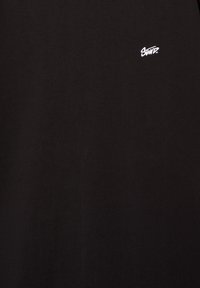 Sort bomulds T-shirt med et lille hvidt broderet logo på venstre bryst. Stoffet er glat med et minimalistisk design.