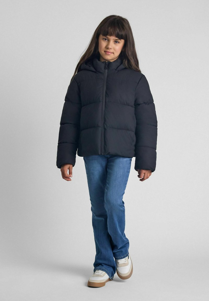 Svart puffjacka med huva, långa ärmar, quiltat mönster, dragkedja fram, bärs över blå jeans och vita sneakers med beige detaljer.