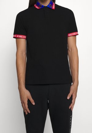Schwarzes Polohemd mit blauem und rotem gemustertem Kragen und roten Bündchen mit der Aufschrift "Versace Jeans Couture." Verfügt über eine klassische Passform und besteht aus Baumwollmaterial.