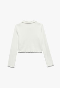 Polo a maniche lunghe, accorciato, di colore bianco, realizzato in tessuto liscio, con colletto e orlo scallopato per una finitura pulita.