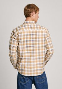 Camicia da uomo a quadri in beige, marrone e blu, con maniche lunghe, polsini bottone e orlo curvo. Tessuto morbido con una finitura testurizzata.