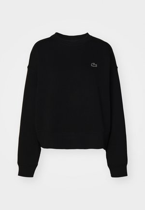 Svart hettegenser med rund hals, senkede skuldre og ribbede mansjetter. Har en liten brodert logo på brystet. Myk stofftekstur.