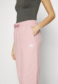 Light pink sweatpants with a soft texture, drawstring waist, side pockets, and white Adidas logo on the left thigh.