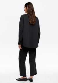 Conjunto negro holgado de dos piezas hecho de tela texturizada; incluye mangas largas, dobladillo redondeado y pantalones de pierna recta, combinado con zapatos planos.